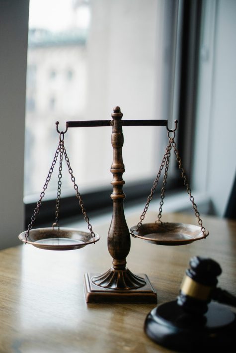 Decorative judgement scale and gavel placed on desk in light lawyer office against window